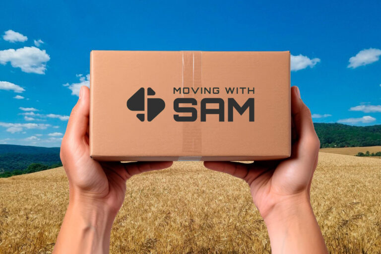 Hands holding a Moving with Sam box over a wheat field